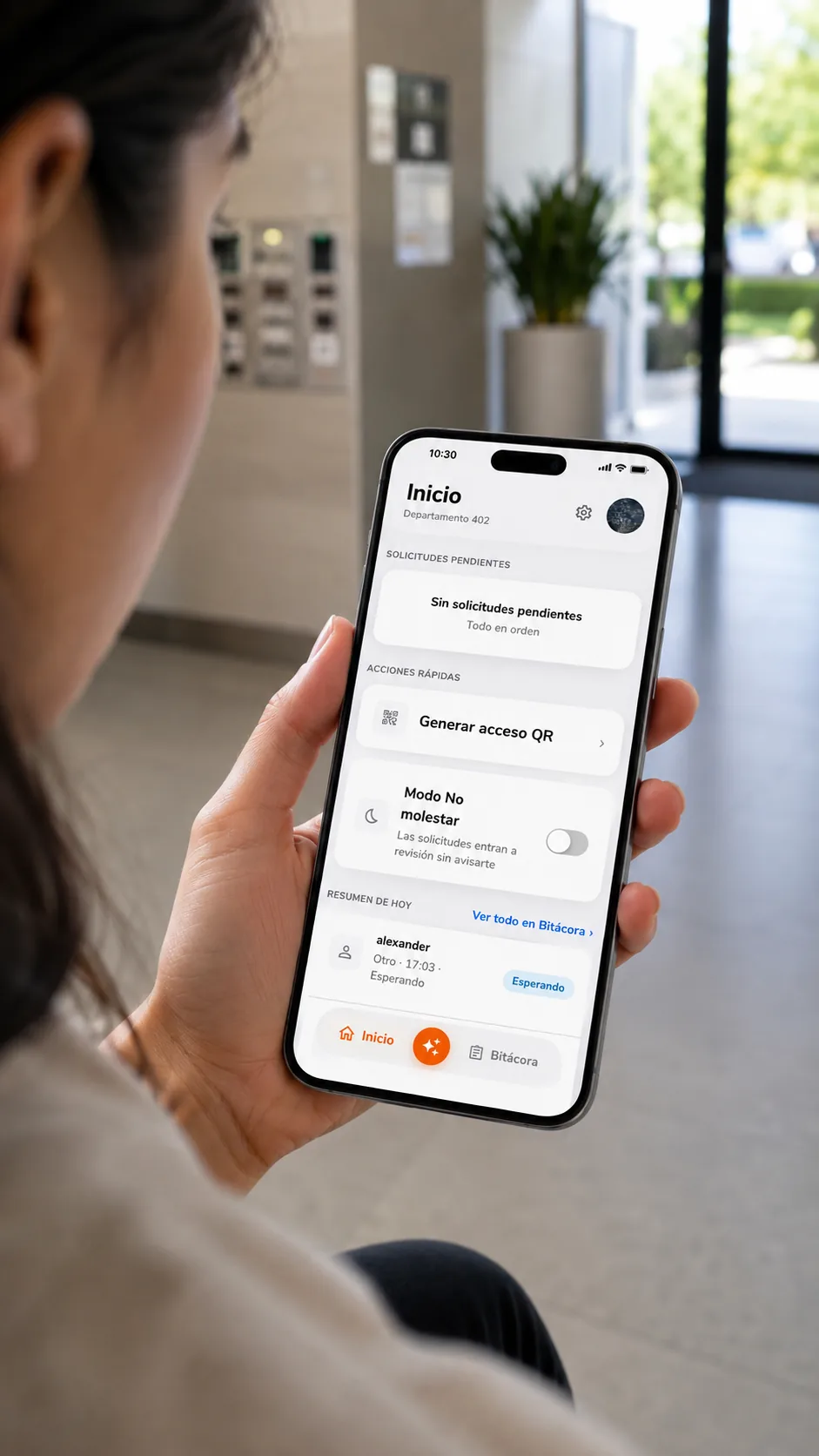 Residente en el lobby del edificio revisando la pantalla de inicio de la app Kigo: solicitudes pendientes, generar acceso QR, modo No molestar y el resumen del día